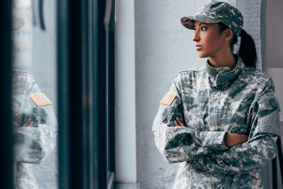 african american woman in military uniform with usa flag emblem looking sad out a window