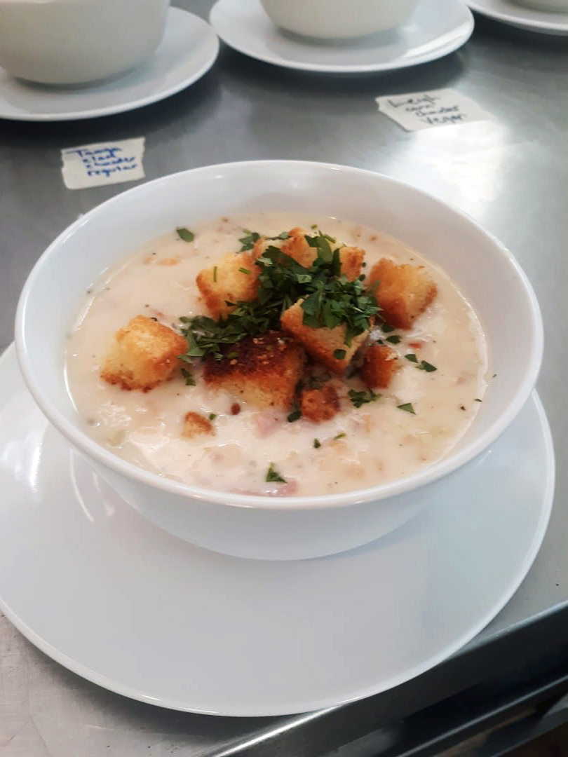 Creamy New England clam chowder crowned with buttery croutons and parsley in a white bowl.
