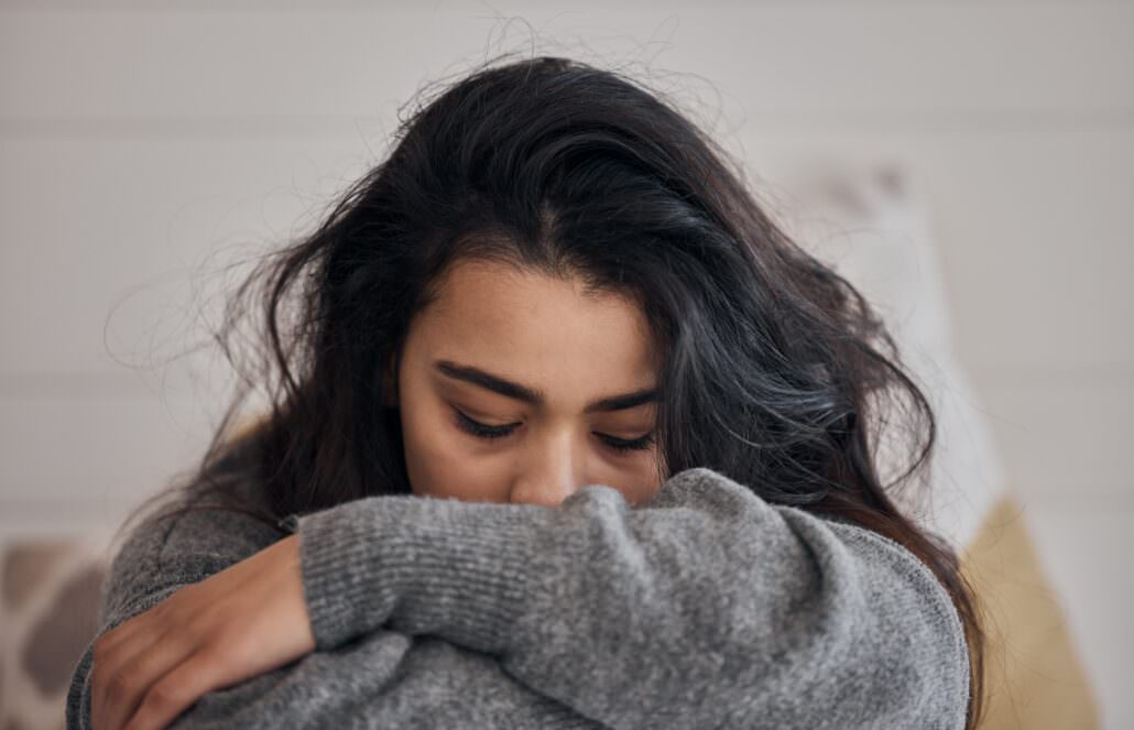 Depressed female veteran in a gray sweater resting head on folded arms in a quiet room.