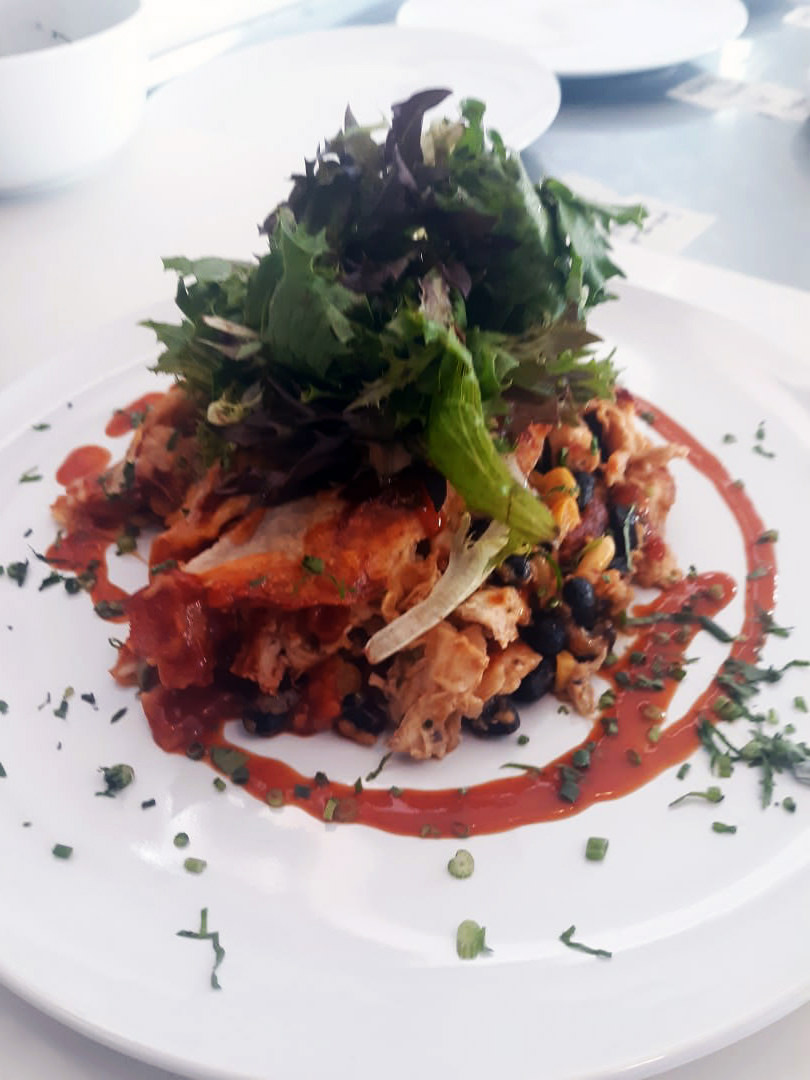 Chicken-black-bean enchilada stack topped with mixed greens, ringed by smoky red sauce.