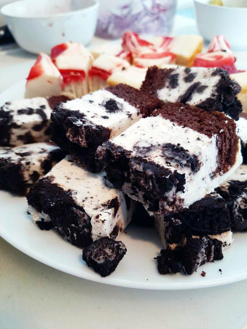 Cookies-and-cream cheesecake brownies stacked beside strawberry-swirl bars.